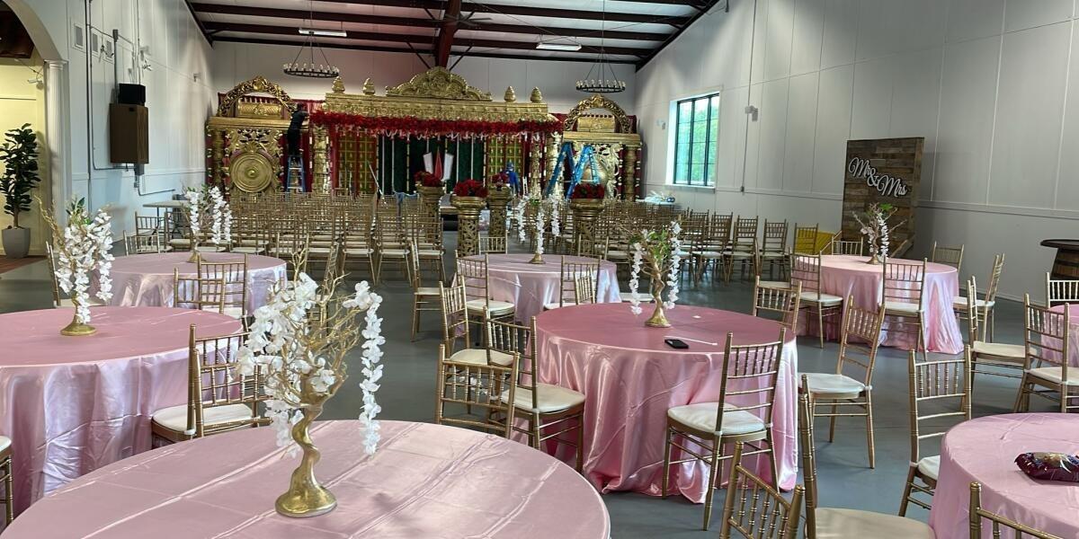 Wedding reception hall at Dream Ranch Events featuring pink round tables, gold chairs, floral centerpieces, and an ornate wedding stage.