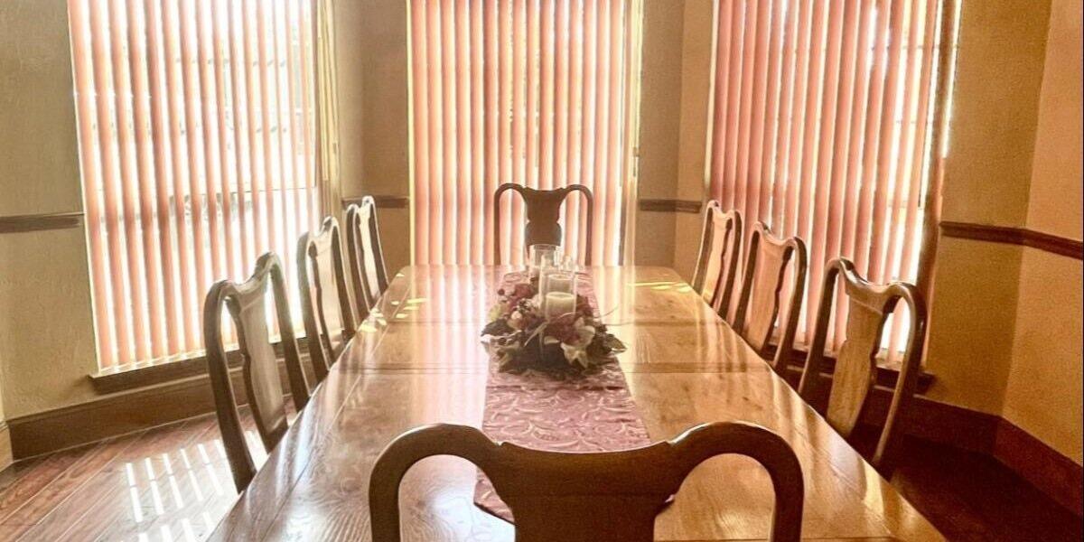 Long wooden dining table with high-back chairs and a floral centerpiece in the formal dining room of the Countryside Home at The Dream Ranch near Dallas