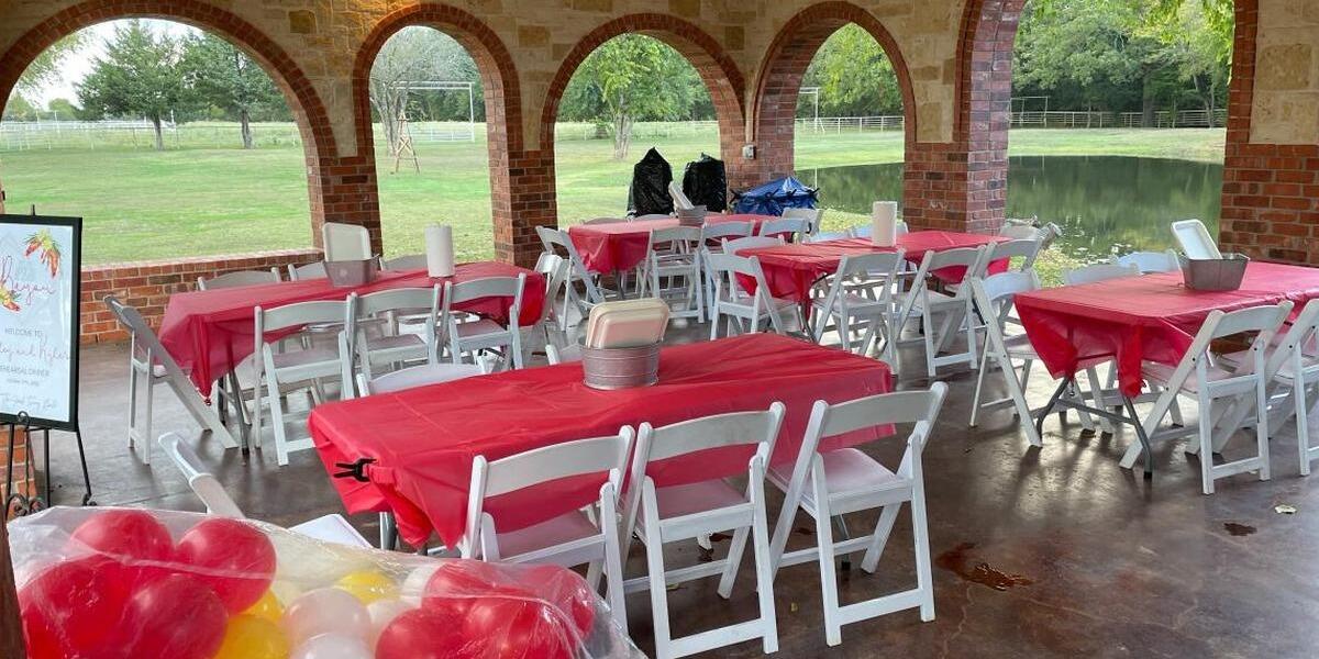 Tables with red cloths, white folding chairs and balloons set inside the Unwind covered gazebo by the pond at The Dream Ranch near Dallas