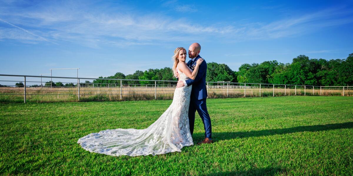 Bride and groom holding hands in front of the wooden triangle arch with red and white flowers at The Avenue ceremony area of The Dream Ranch near Dallas